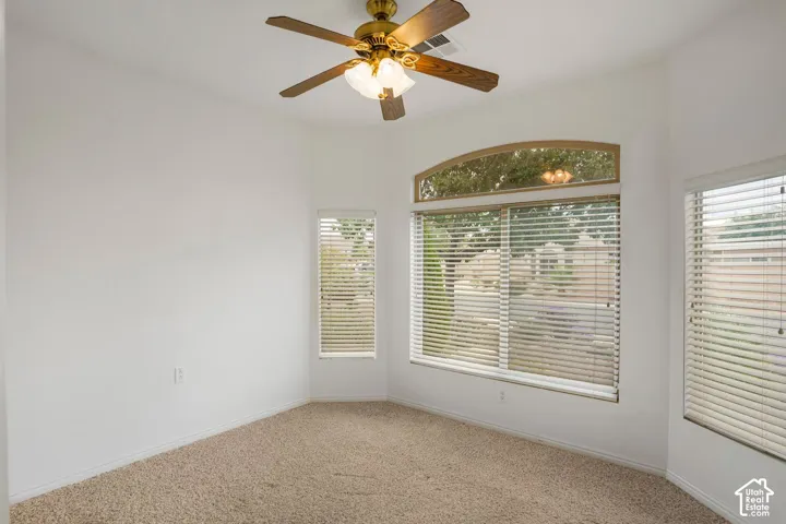 Textured wall-to-wall carpeting, ceiling fan with integrated lighting, and multiple windows including an arched transom window