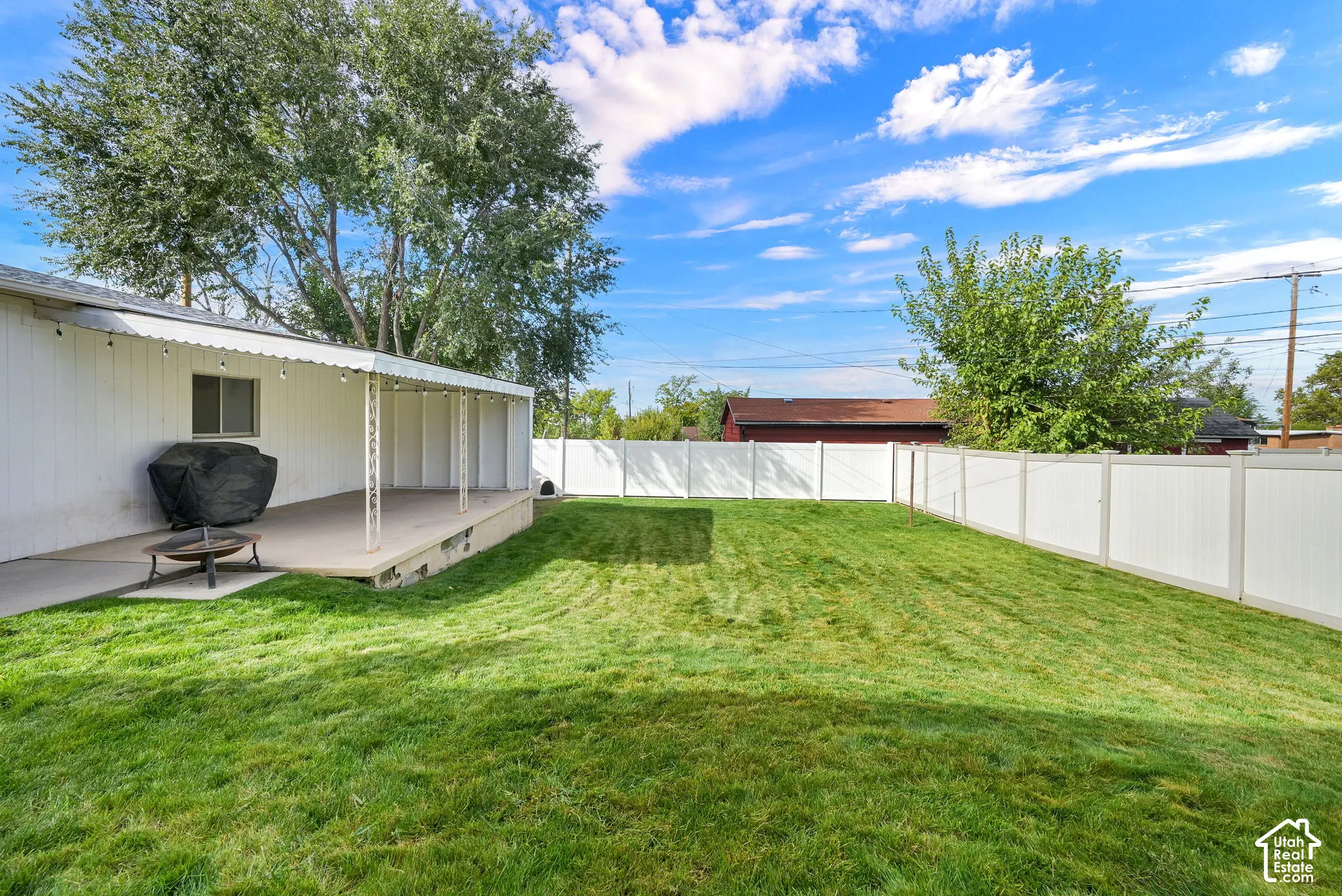 Backyard featuring a concrete patio, a covered porch, a manicured lawn, and a full-perimeter white vinyl fence