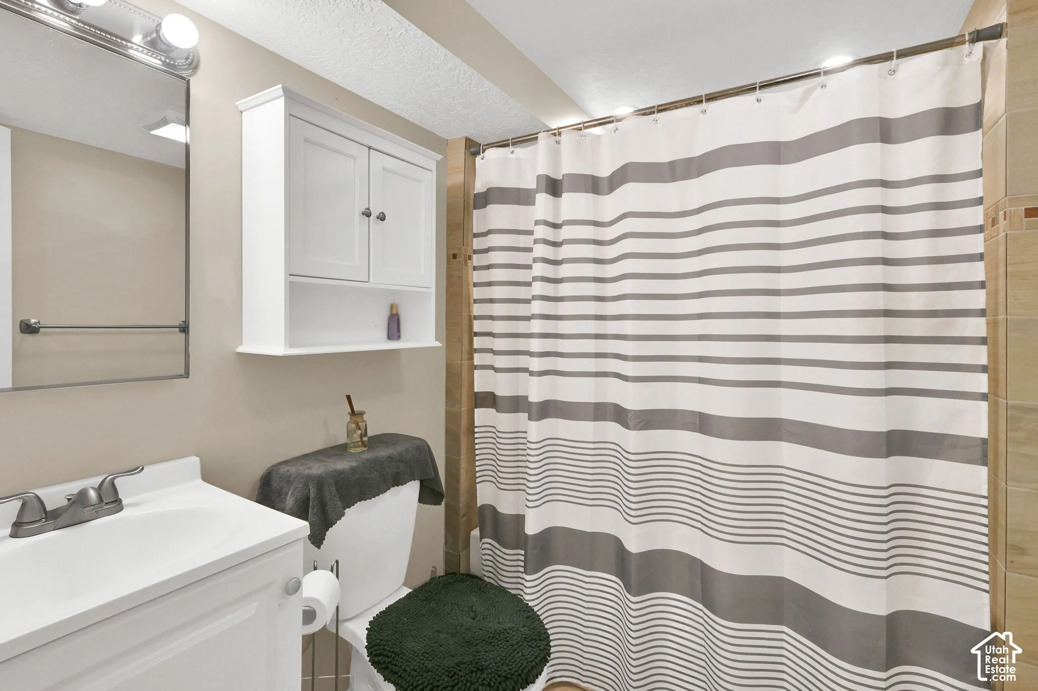 Bathroom featuring a white vanity cabinet, wall-mounted storage cabinet, framed mirror, and tile shower surround