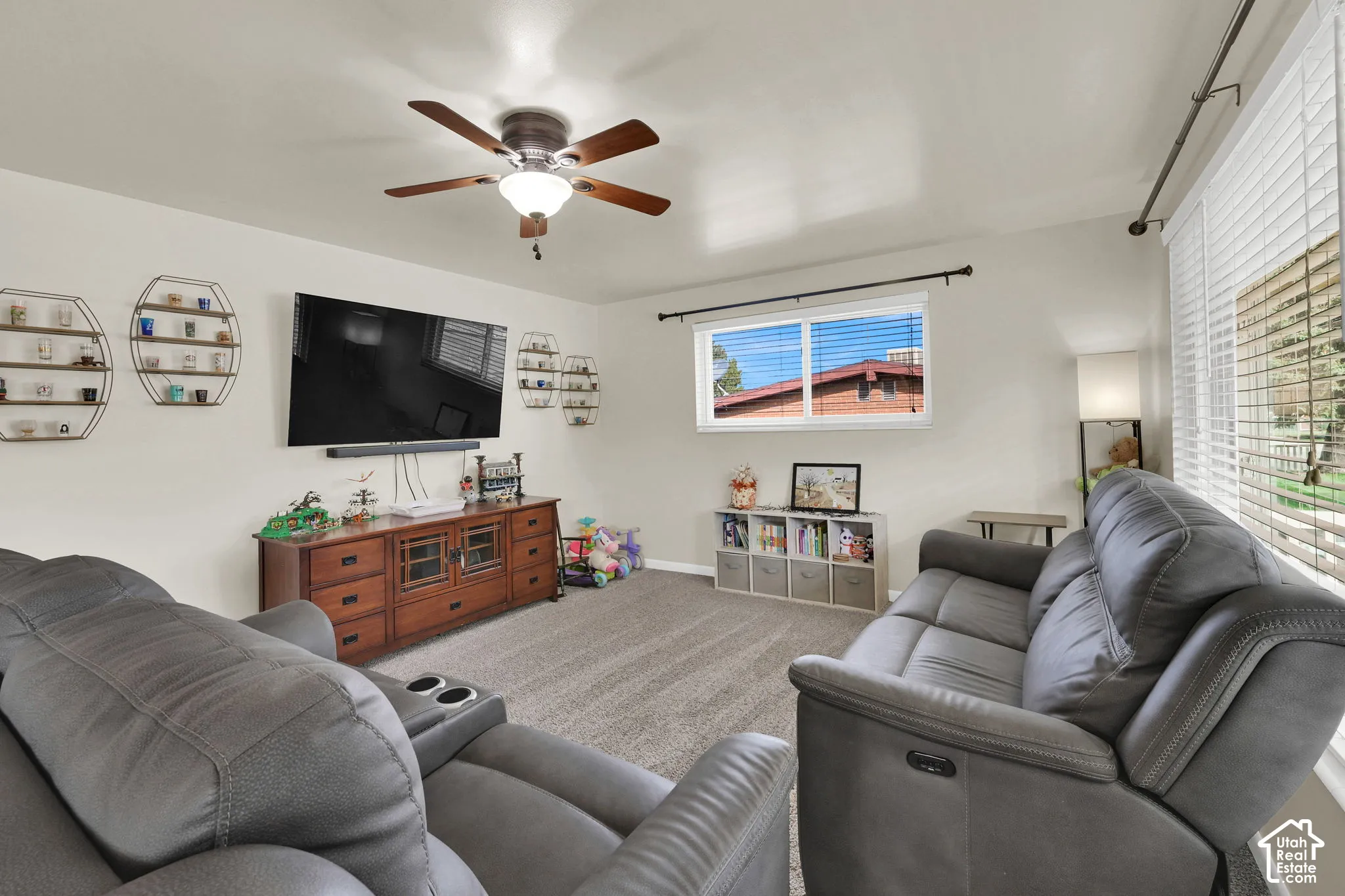 Living space featuring neutral wall paint, carpeted flooring, a ceiling fan with integrated lighting, and horizontal window blinds