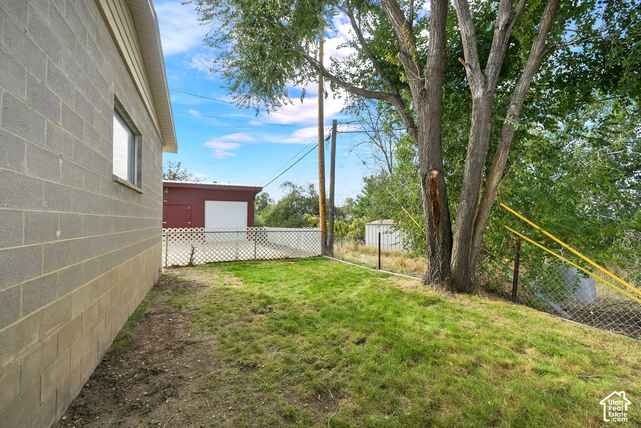 Exterior yard area featuring concrete block siding, mature trees, and a detached structure with a single garage bay
