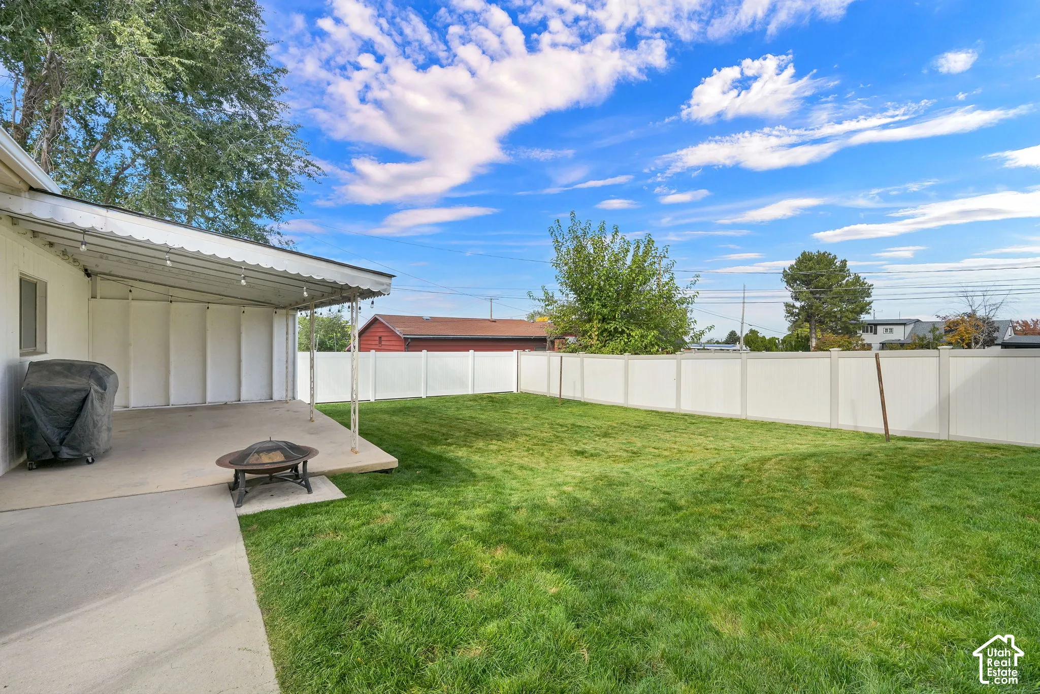 Covered concrete patio, fenced backyard, and manicured lawn