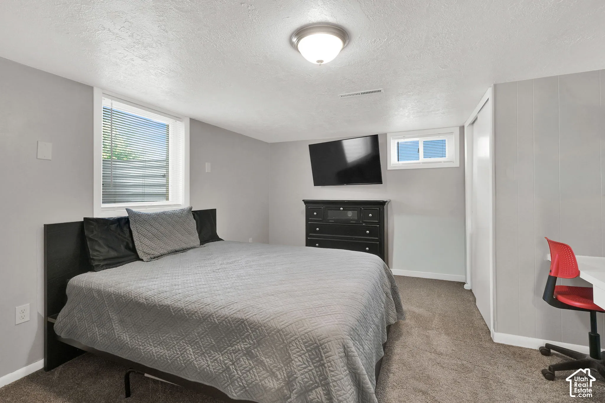 Neutral-toned room featuring carpeted flooring, two casement windows, a ceiling-mounted light fixture, and a built-in closet with sliding doors