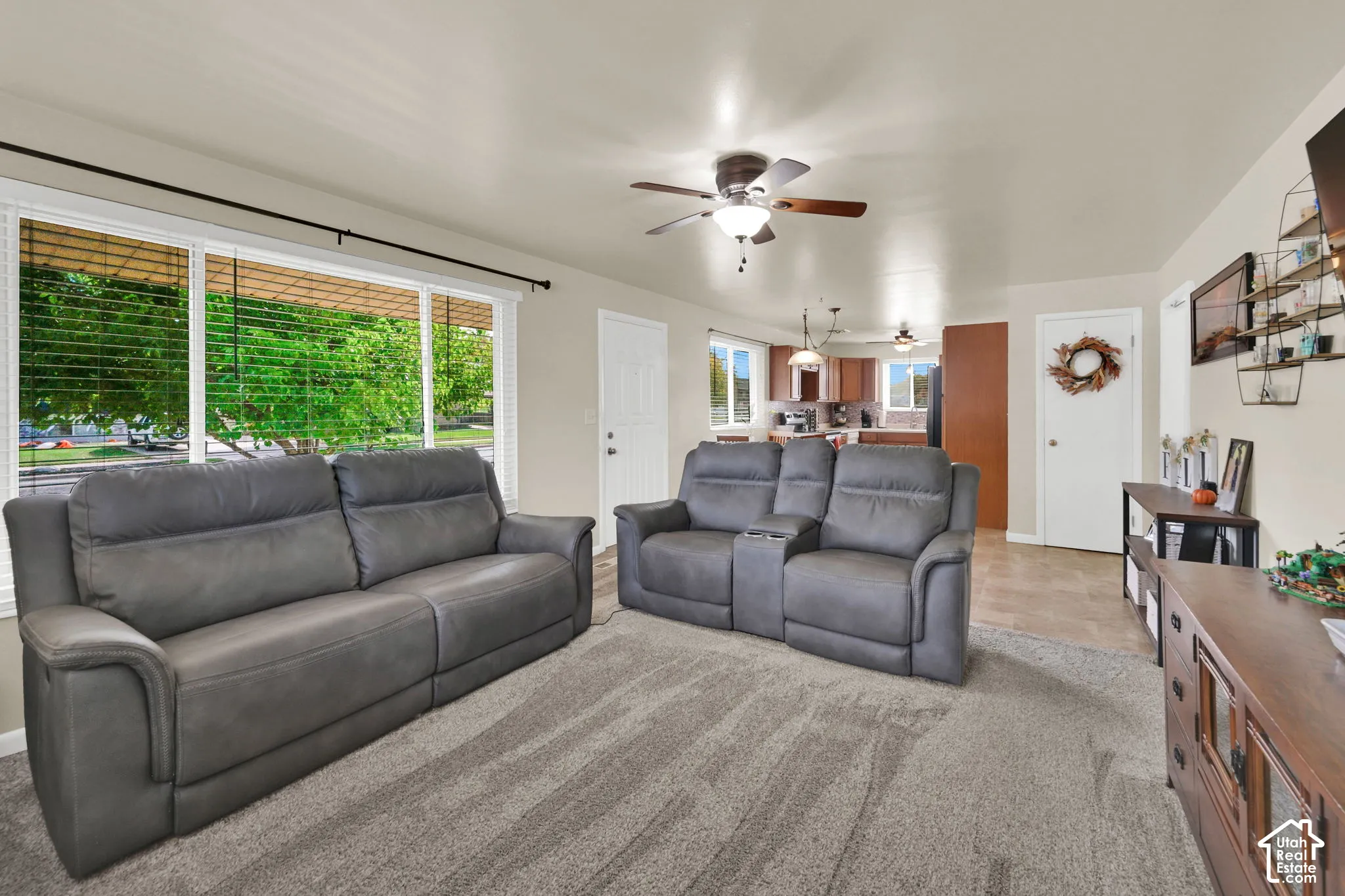 Living area featuring large windows, neutral wall tones, carpet flooring, and a ceiling fan with integrated lighting