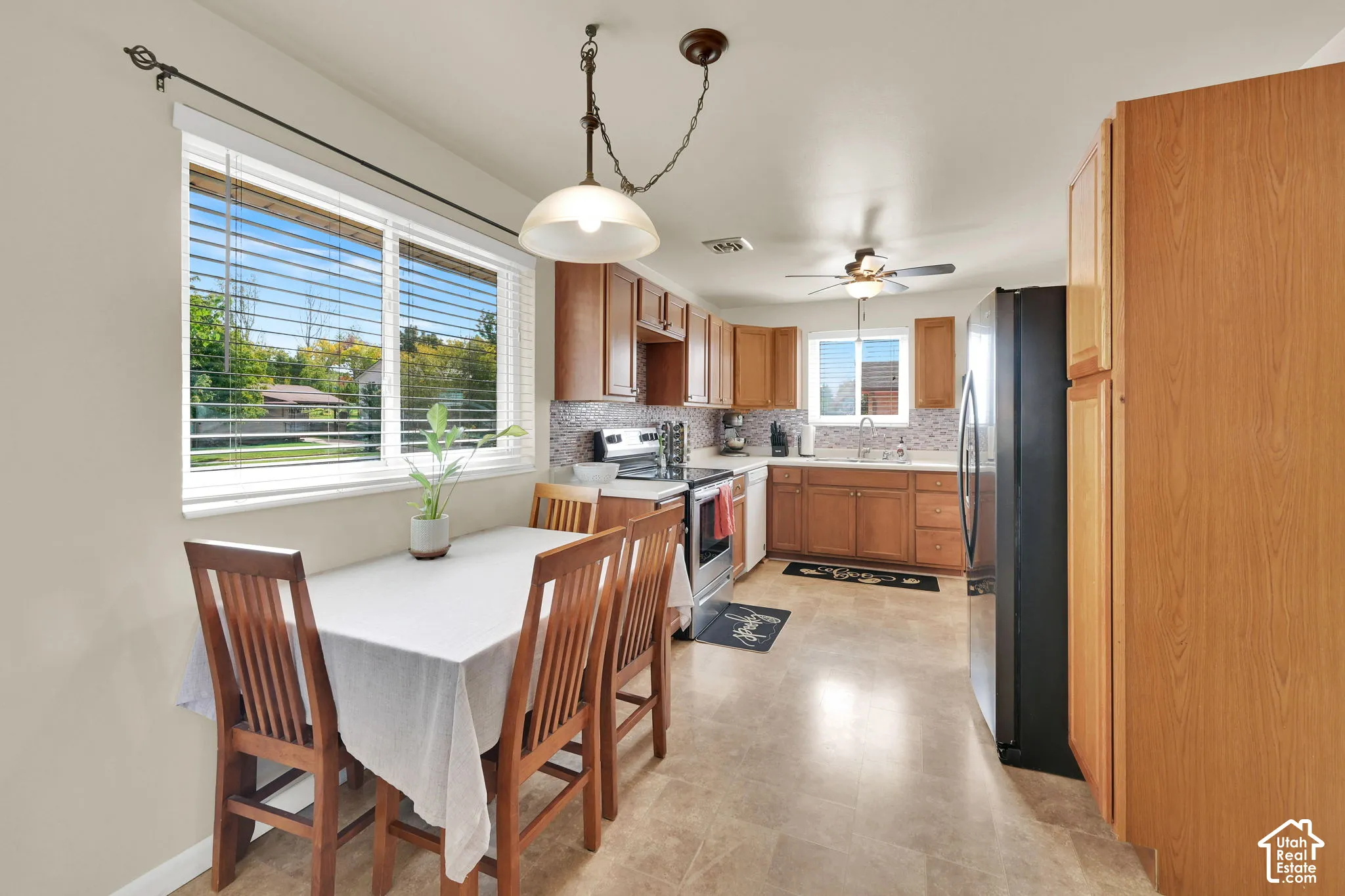 Kitchen featuring wood cabinetry, tile flooring, stone-tiled backsplash, stainless steel appliances, and a hanging pendant light fixture