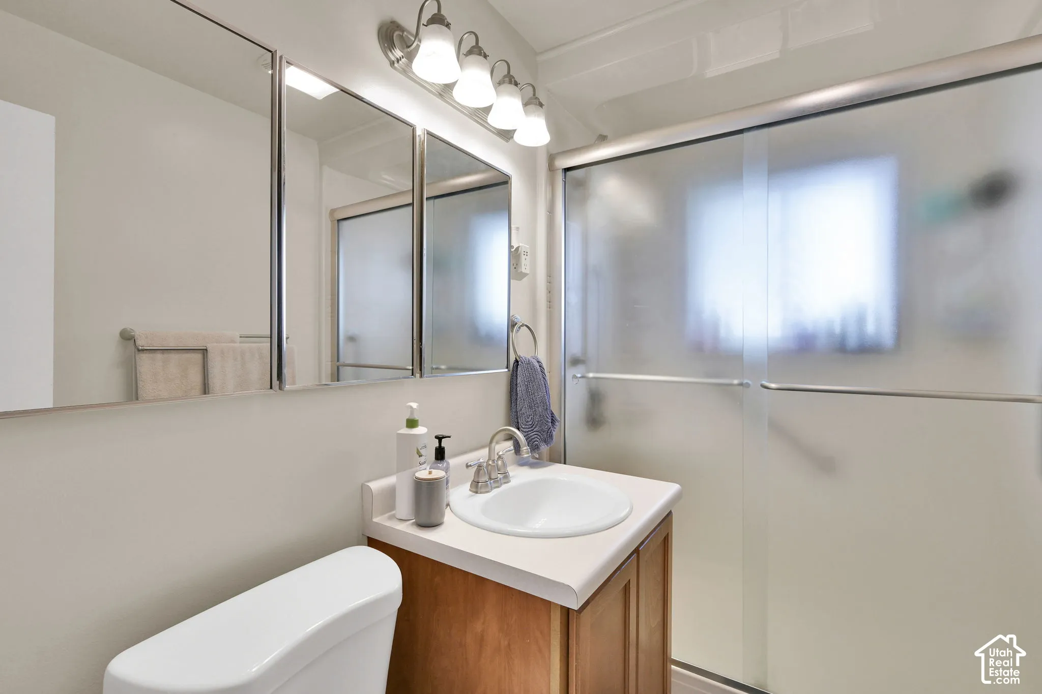 Bathroom vanity with wood-finish cabinetry, countertop with integrated sink, chrome faucet, expansive wall-mounted mirror, and glass-enclosed shower