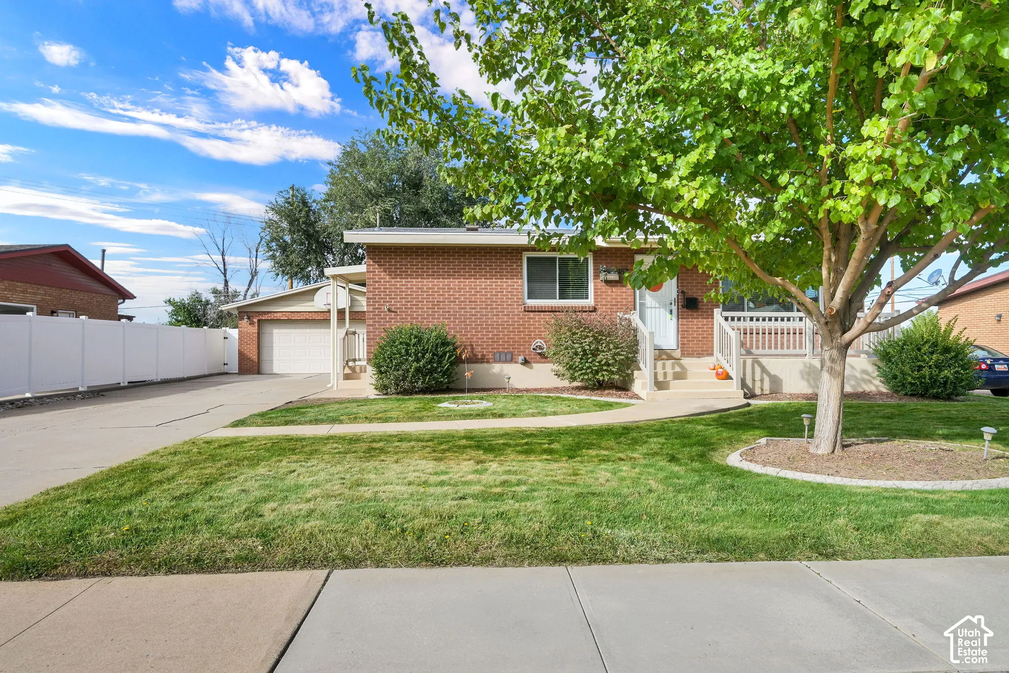 Brick exterior featuring a concrete driveway, detached garage, elevated front porch with railing, and white vinyl perimeter fencing