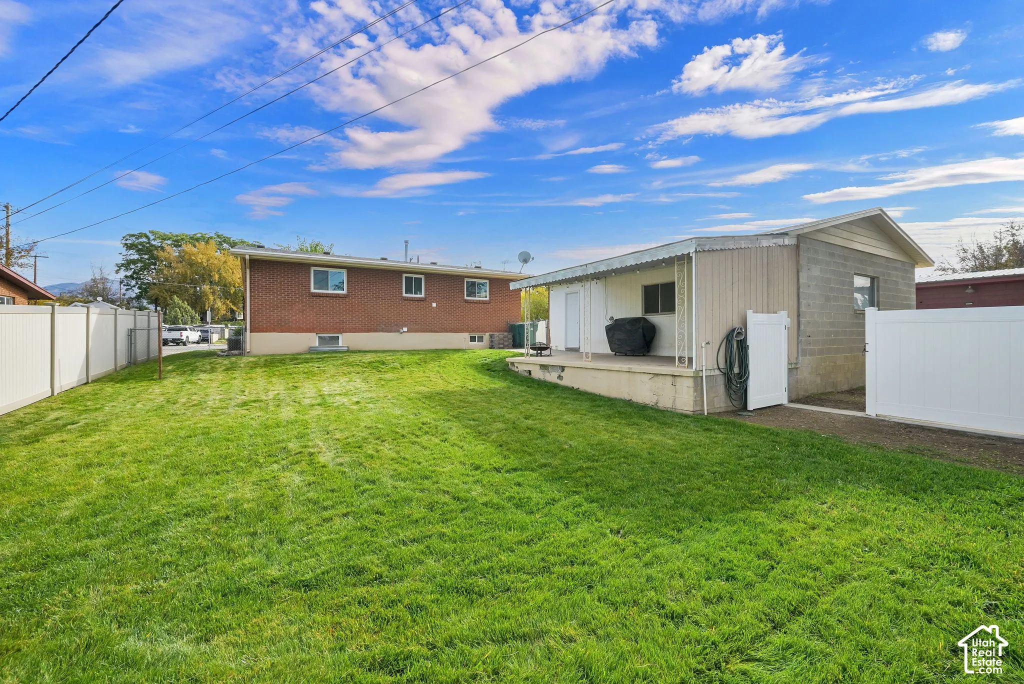 Backyard featuring a grass lawn, a covered concrete patio, and white vinyl perimeter fencing
