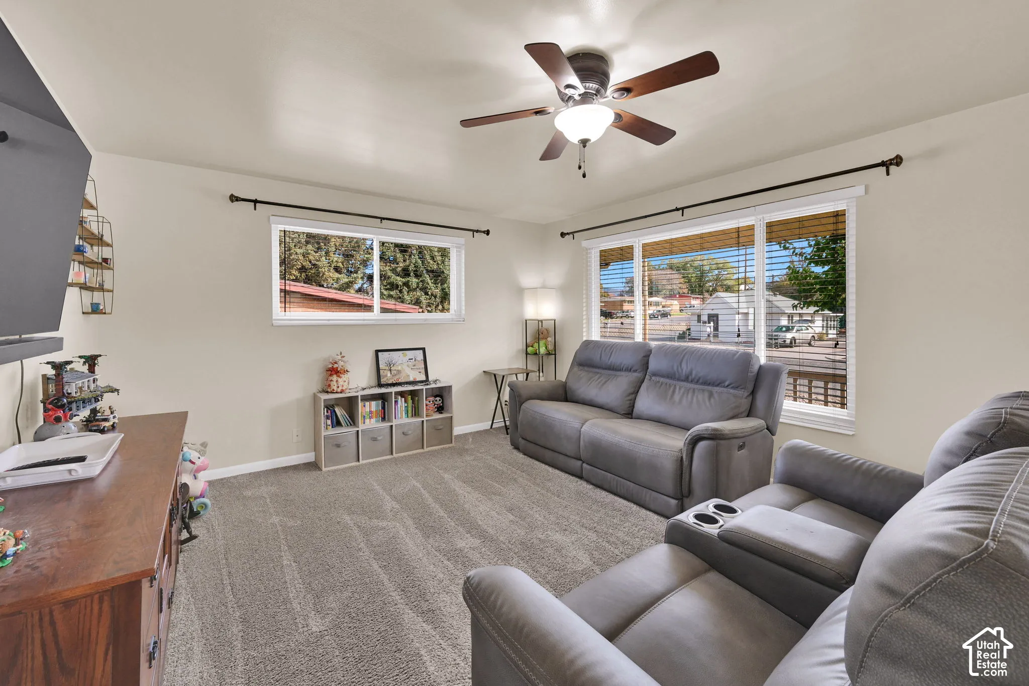 Neutral interior space featuring wall-to-wall carpeting, large windows with curtain rods, and a ceiling fan with integrated lighting