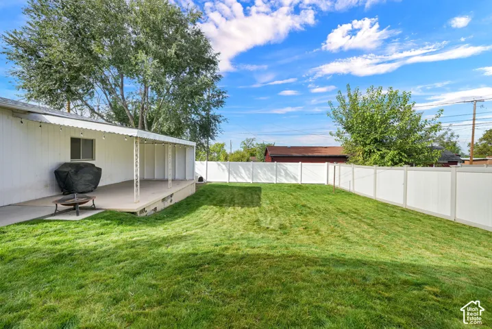 Backyard featuring a concrete patio, a covered porch, a manicured lawn, and a full-perimeter white vinyl fence