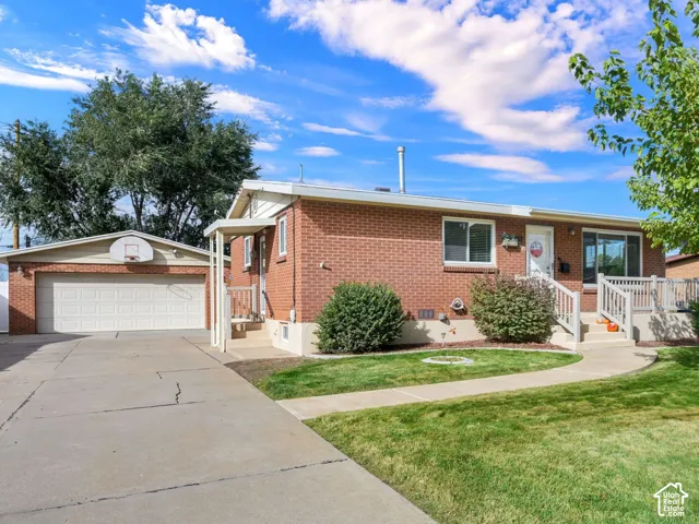Brick exterior, detached two-car garage, concrete driveway, front deck with railings, and manicured lawn