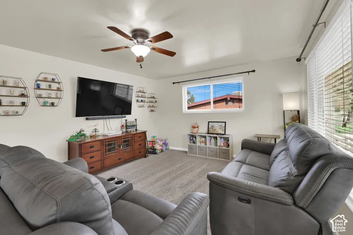 Living space featuring neutral wall paint, carpeted flooring, a ceiling fan with integrated lighting, and horizontal window blinds