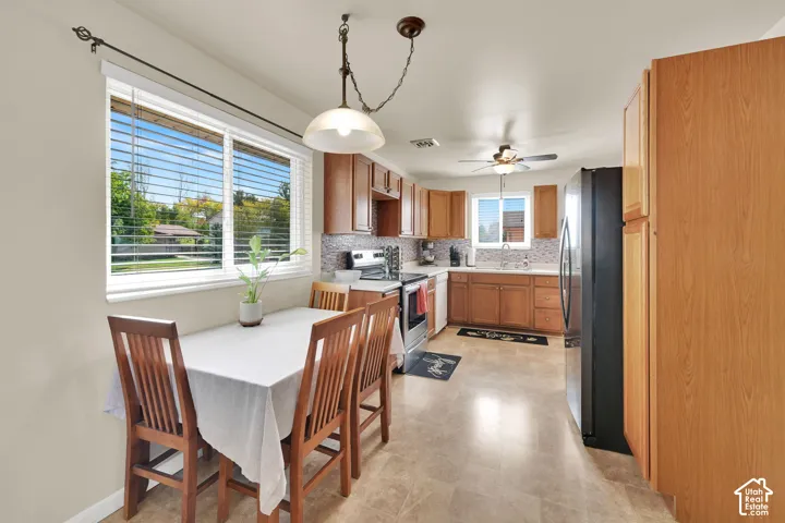 Kitchen featuring wood cabinetry, tile flooring, stone-tiled backsplash, stainless steel appliances, and a hanging pendant light fixture