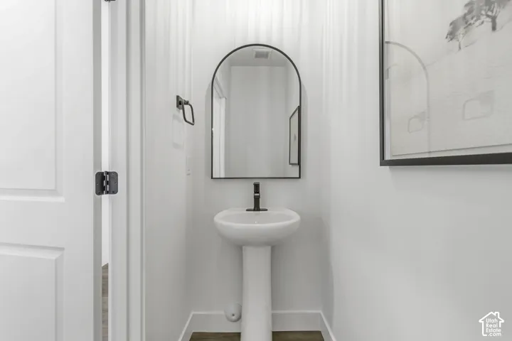 Pedestal sink featuring a single-handle dark metal faucet, arched wall-mounted mirror, and dark metal towel ring