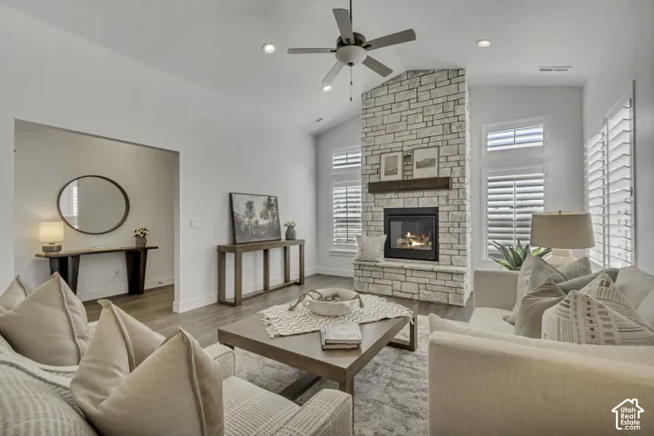 Living area featuring vaulted ceilings, stone-surround fireplace with a wooden mantel, wood-finish flooring, recessed lighting, and windows with interior plantation shutters