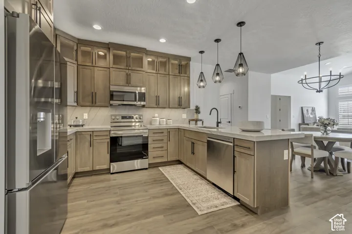 Kitchen featuring shaker-style cabinetry with glass-front uppers, stainless steel appliances, quartz countertops, a central island with an integrated sink, and wood-finish flooring