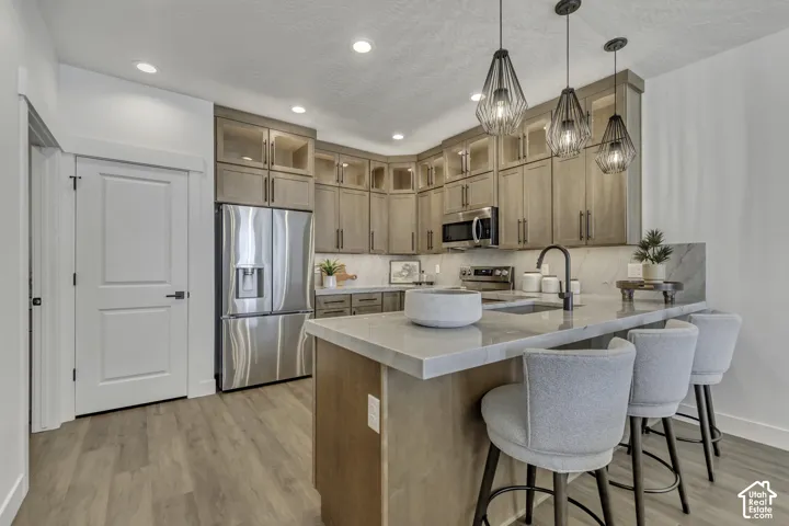 Kitchen featuring light wood-finish cabinetry, quartz countertops, stainless steel appliances, geometric pendant lighting, and wood-finish flooring