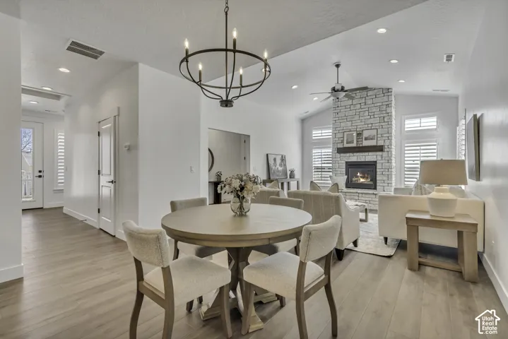 Open-concept area featuring wood-finish flooring, vaulted ceilings, a stone-faced fireplace with a wood mantel, a contemporary wrought-iron chandelier, and recessed lighting