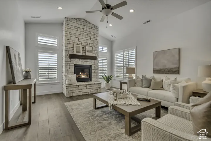 Vaulted ceiling featuring a central stone-clad fireplace, wood-finish flooring, recessed lighting, and windows finished with plantation shutters