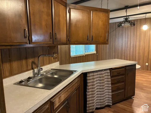 Kitchen featuring wood cabinetry, solid-surface countertops, dual-basin stainless steel sink with high-arc faucet, and decorative metal pendant lighting