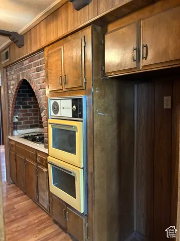 Kitchen featuring wood-finish cabinetry, a brick arched cooktop alcove, and a built-in dual oven