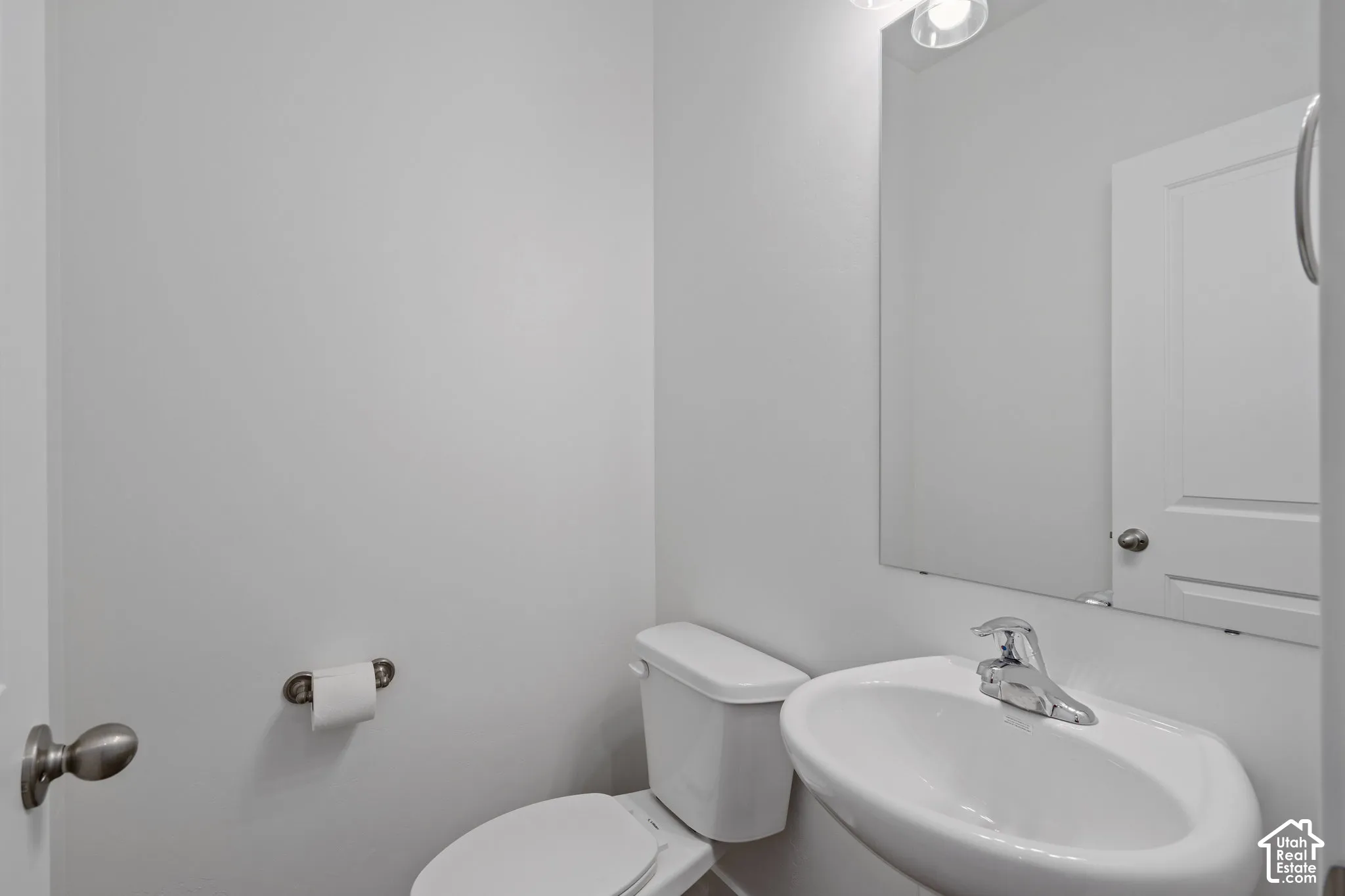 Powder room featuring a pedestal sink, chrome faucet, wall-mounted mirror, and a two-piece toilet