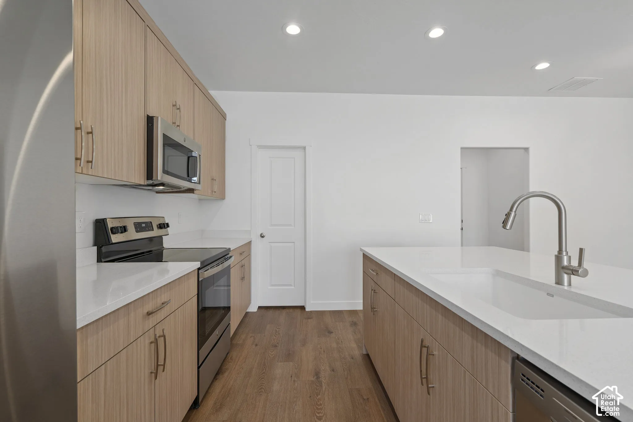 Modern kitchen featuring light-toned wood melamine cabinetry,  wood-finish LVP flooring, stainless steel appliances, and a recessed kitchen sink with an arched faucet