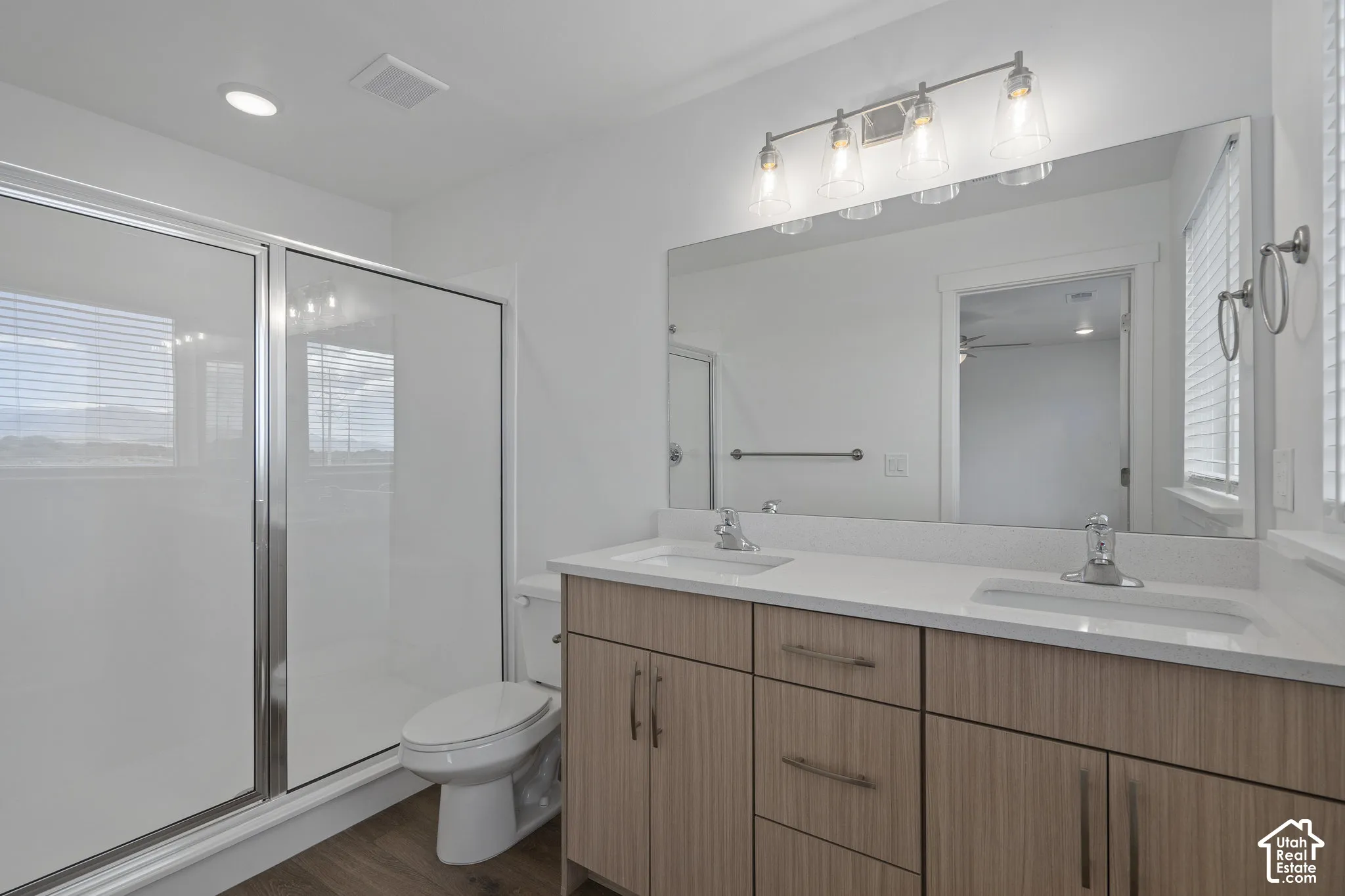 Double vanity with a light wood-finish melamine cabinet, quartz countertop, dual drop-in sinks, full-width mirror, and four-light glass shade fixture