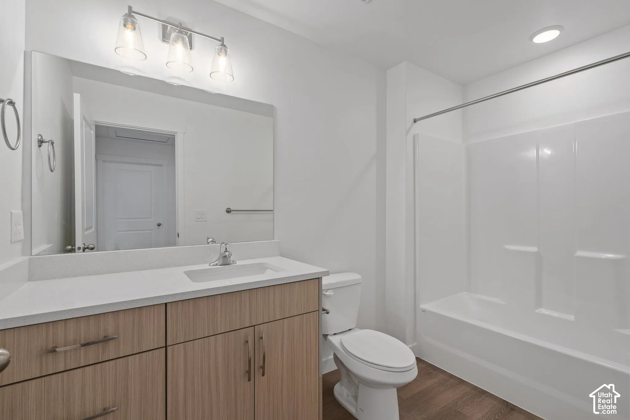 Bathroom featuring wood-finish melamine cabinetry, white solid-surface countertop with an integrated sink, full-width vanity mirror, three-light fixture, and a tub-shower combination with a surround