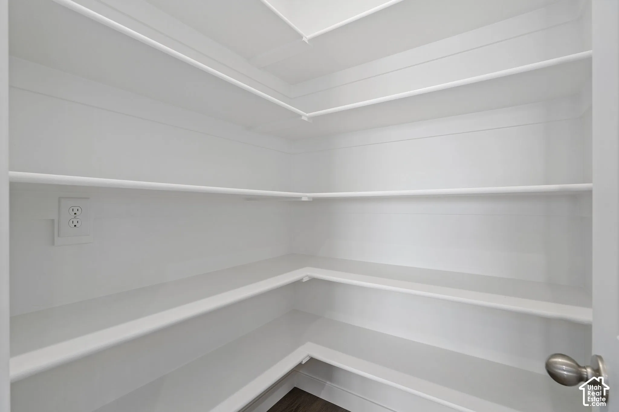 Storage area featuring wrap-around tiered shelving, bright white painted interior, and a built-in electrical outlet
