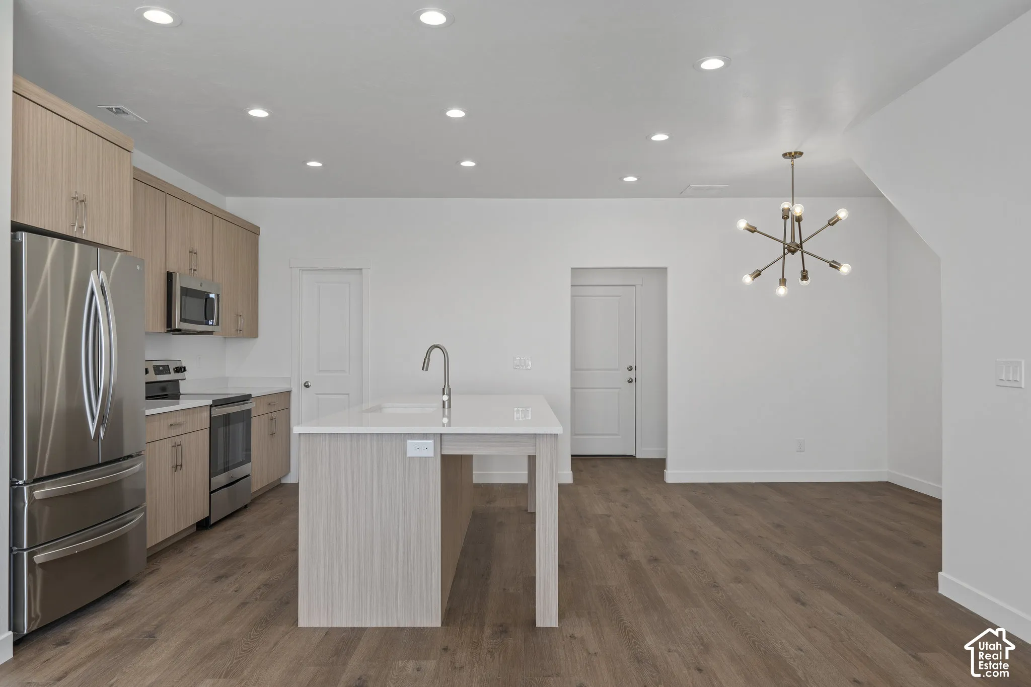 Kitchen featuring light-finish melamine cabinetry, a central island with a quartz countertop, wood-finish flooring, stainless steel appliances, and multi-arm chandelier lighting