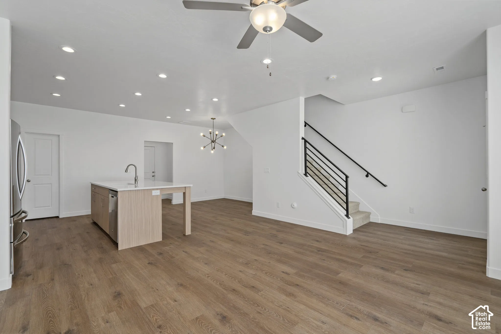 Open floor plan featuring LVP wood-finish flooring, recessed lighting, a kitchen island with a neutral-tone finish, and a staircase with a black metal railing