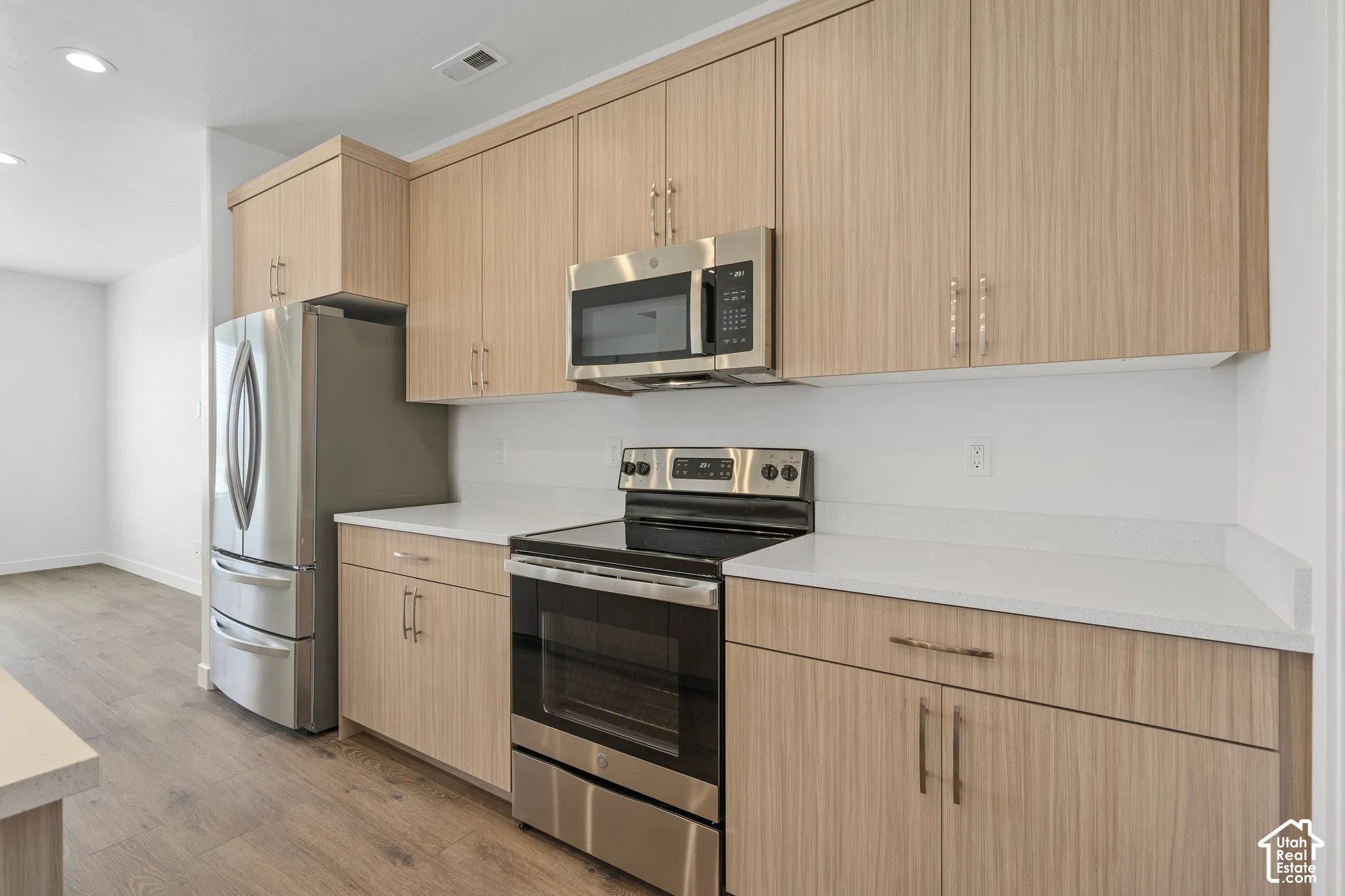 Kitchen featuring light melamine cabinetry, stainless steel appliances, solid surface countertops, and wood-finish flooring