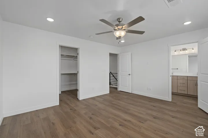 Room featuring LVP wood-finish flooring, recessed lighting, a multi-blade ceiling fan with an integrated light fixture, a walk-in closet, and a bathroom with a melamine wood-finish vanity