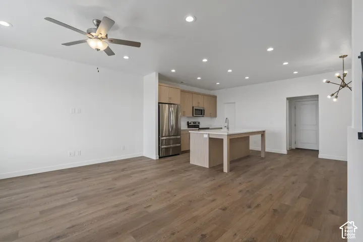Open kitchen featuring wood-finish cabinetry, a center island with a stone-surface countertop, stainless steel appliances, recessed lighting, and wood-finish flooring