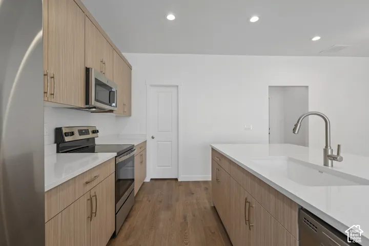Modern kitchen featuring light-toned wood melamine cabinetry,  wood-finish LVP flooring, stainless steel appliances, and a recessed kitchen sink with an arched faucet