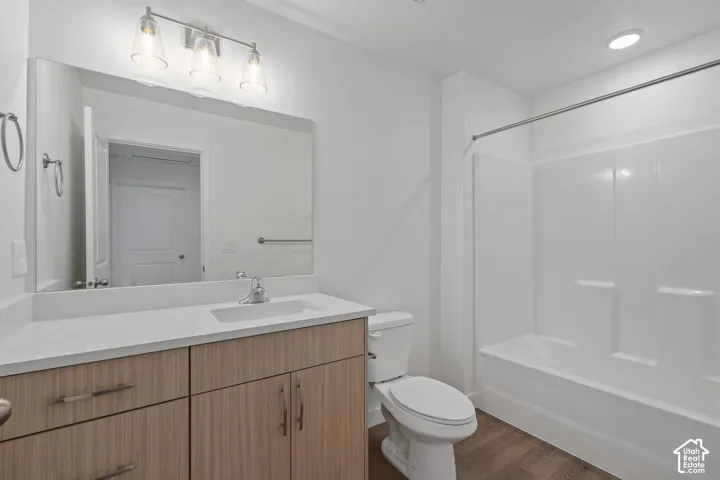 Bathroom featuring wood-finish melamine cabinetry, white solid-surface countertop with an integrated sink, full-width vanity mirror, three-light fixture, and a tub-shower combination with a surround