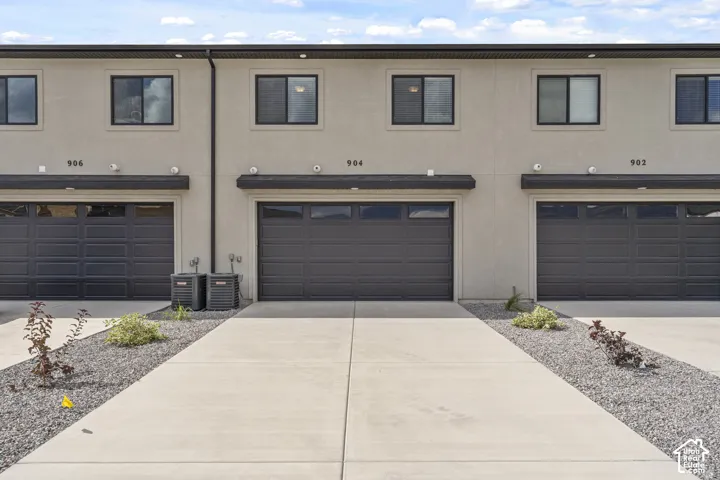 Multi-unit exterior featuring a smooth stucco facade, dark-toned garage doors with inset windows, concrete driveways, and stone-ground landscaping