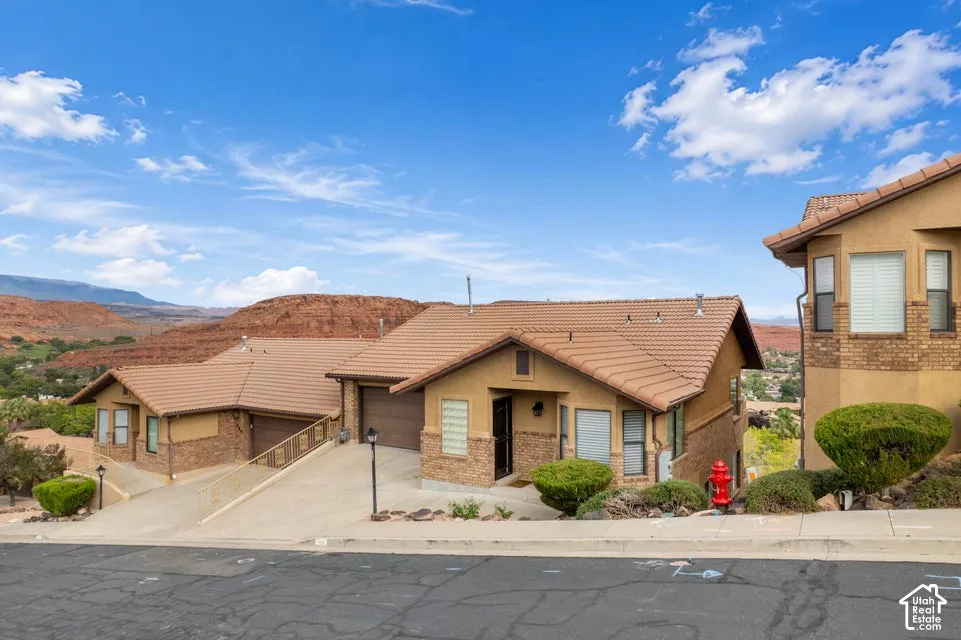 Exterior facade featuring tan stucco, stone veneer accents, and a multi-gabled tile roof, complemented by an attached garage and desert landscape backdrop