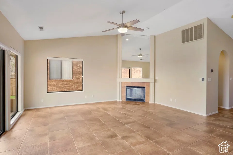 Vaulted ceiling featuring a ceiling fan, ceramic tile flooring, a fireplace with a tiled surround, a floor-to-ceiling wall mirror, and sliding glass doors