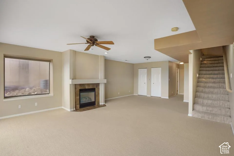 Carpeted living space featuring a fireplace with a stone-tile surround, a built-in mantle, a ceiling fan, and a staircase with a handrail