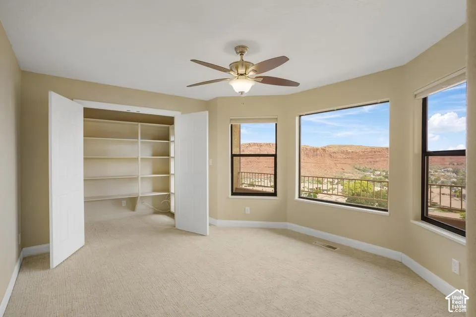 Bay windows with mountain landscape scenery, built-in shelving, carpeted flooring, and a ceiling fan with integrated lighting
