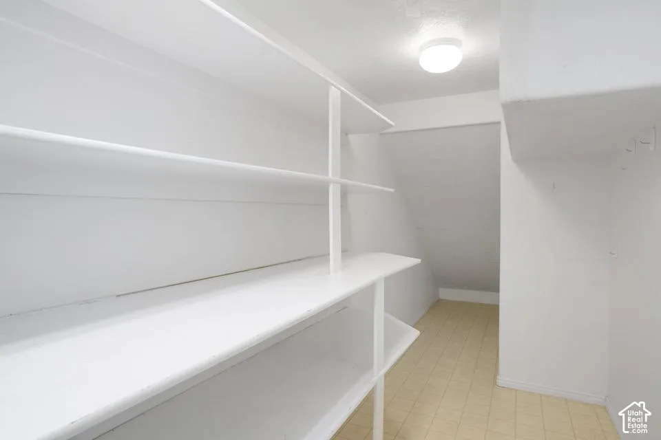 Storage area featuring multi-tier fixed shelving, neutral tile flooring, and a flush-mount ceiling light fixture