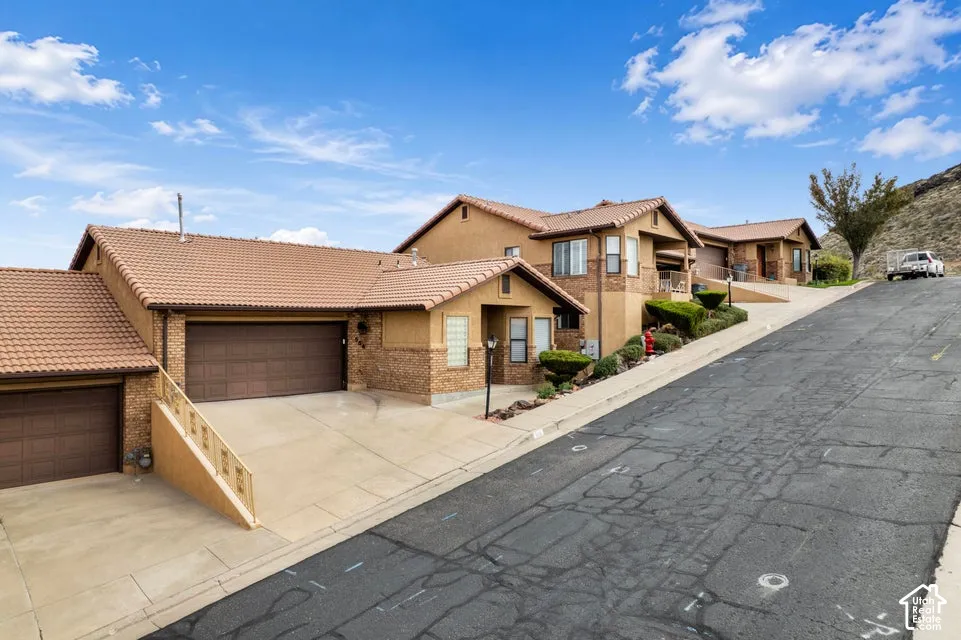 Stucco exterior with stone veneer accents, multi-level tiled roofing, and two attached garages with concrete driveways