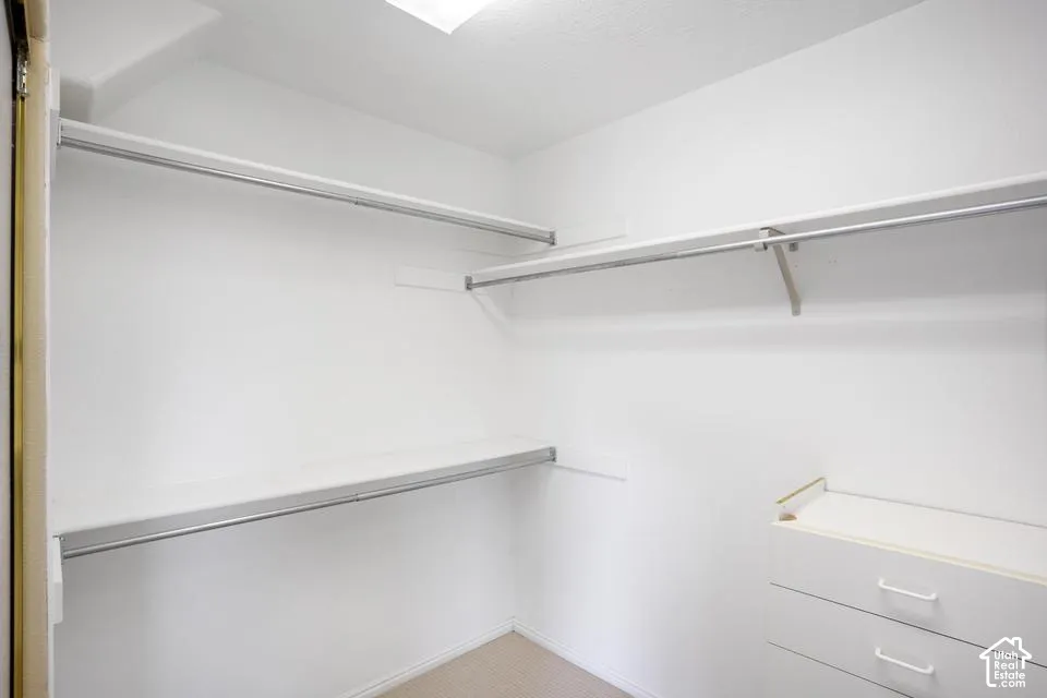 Storage space featuring tiered shelving, integrated clothing rods, and a built-in cabinetry unit with three drawers