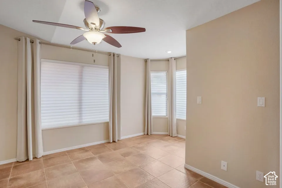 Neutral-toned interior space featuring ceramic tile flooring, a multi-blade ceiling fan with an integrated light fixture, and large windows with integrated blinds