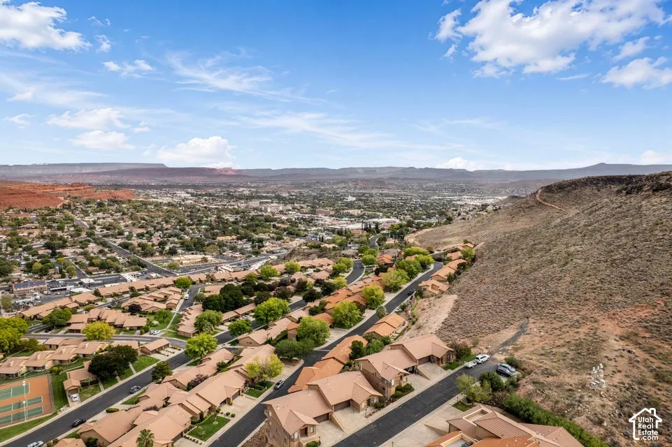 Aerial perspective of a residential neighborhood featuring mountain topography, desert landscaping, paved streets, and tennis courts