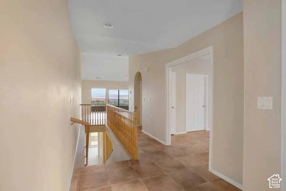 Hallway featuring ceramic tile flooring, a wood-spindle railing, and a decorative arched passage