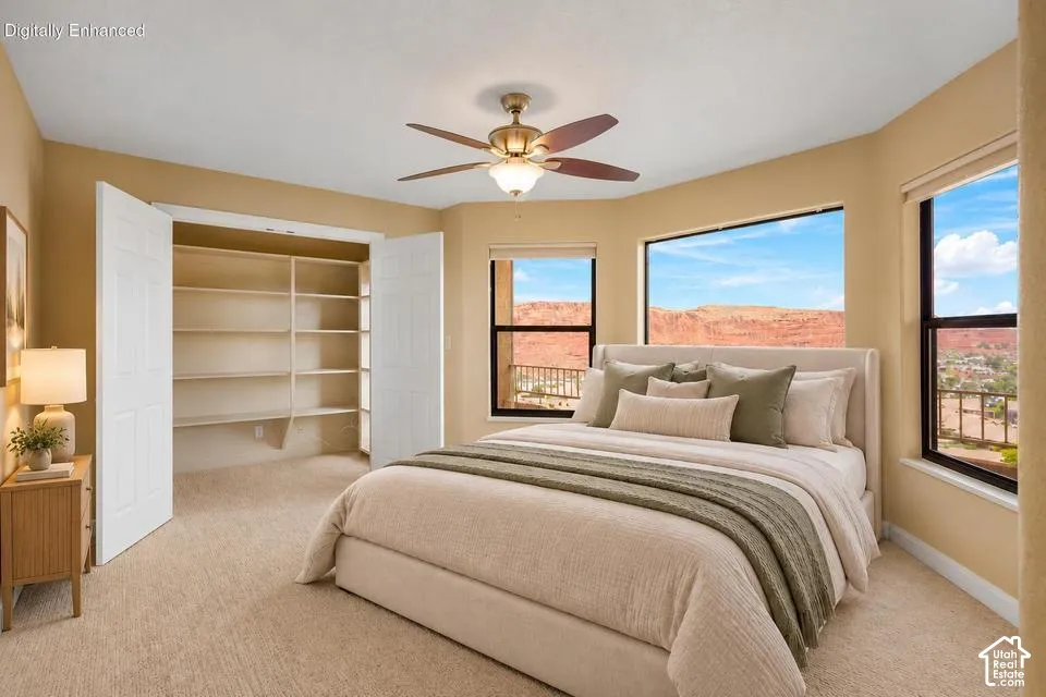 Room featuring expansive windows, red rock mountain scenery, built-in closet shelving, neutral carpeting, and a ceiling fan with integrated lighting