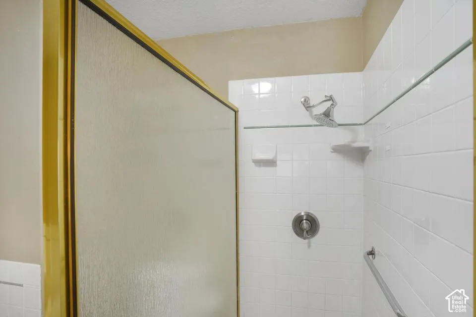 Shower enclosure featuring white wall tiling, a gold-trimmed frame, a metallic showerhead, built-in soap dish, and a metallic wall-mounted grab bar